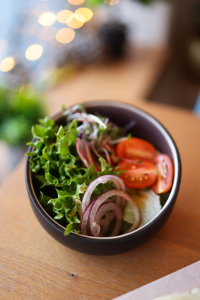 HOME Close-up of a fresh salad bowl with lettuce, tomato, and onion slices on a wooden table.
