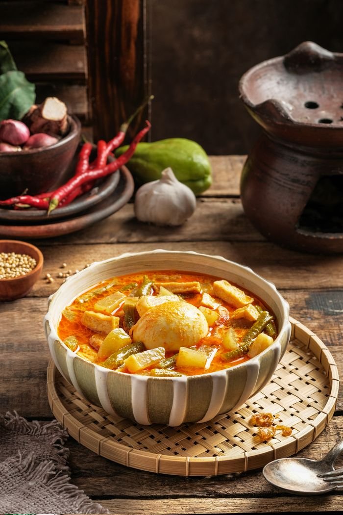 HOME A bowl of flavorful Lontong Sayur with vegetables and egg, showcasing Indonesian cuisine.
